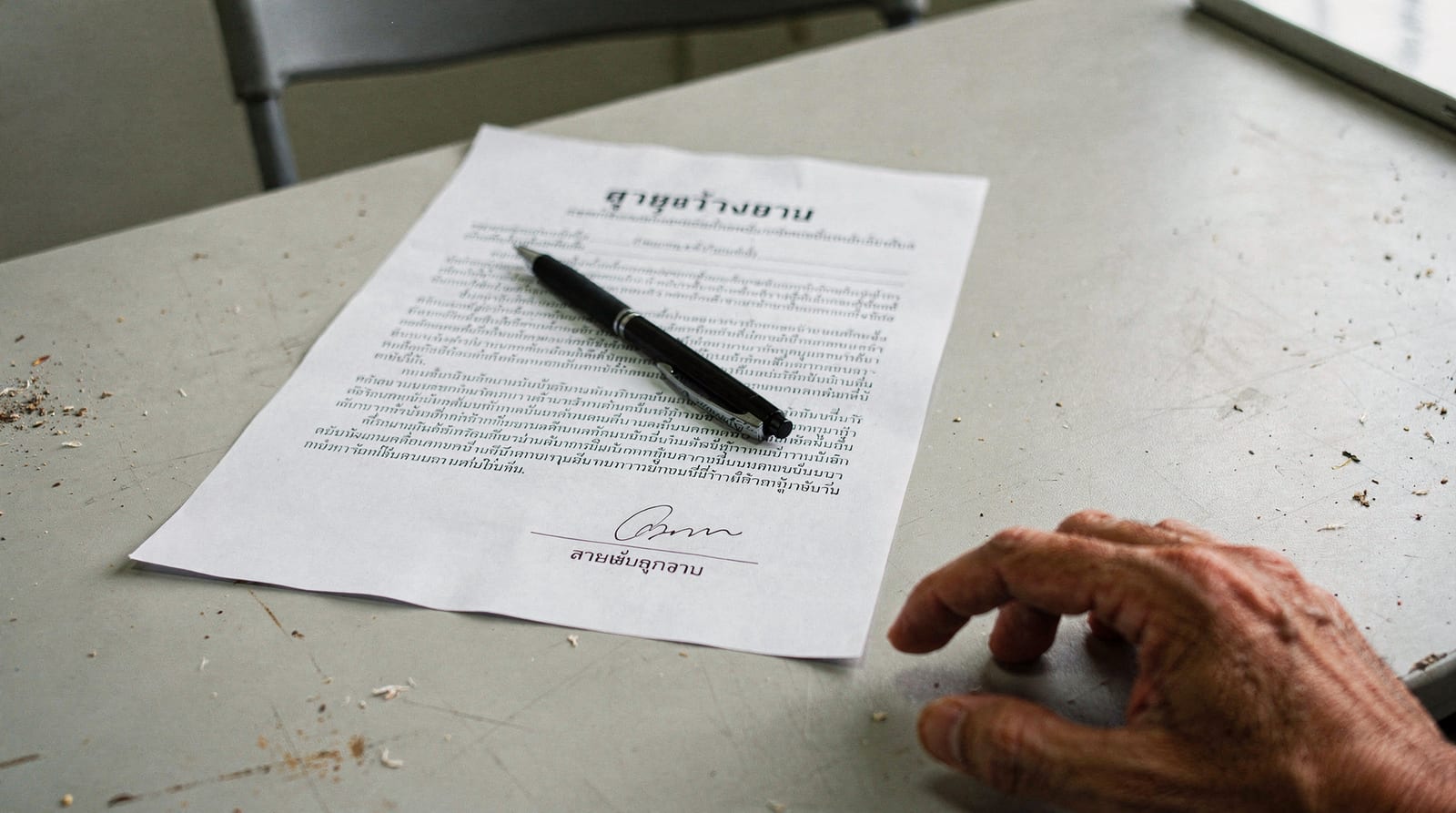A Thai employment contract on a table with a pen ready for signature and a hand resting at the edge.